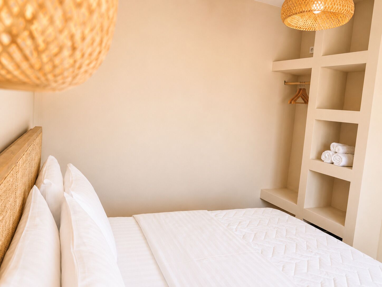 Een netjes opgemaakt bed met witte lakens, een geweven hoofdbord en een hangende lamp.