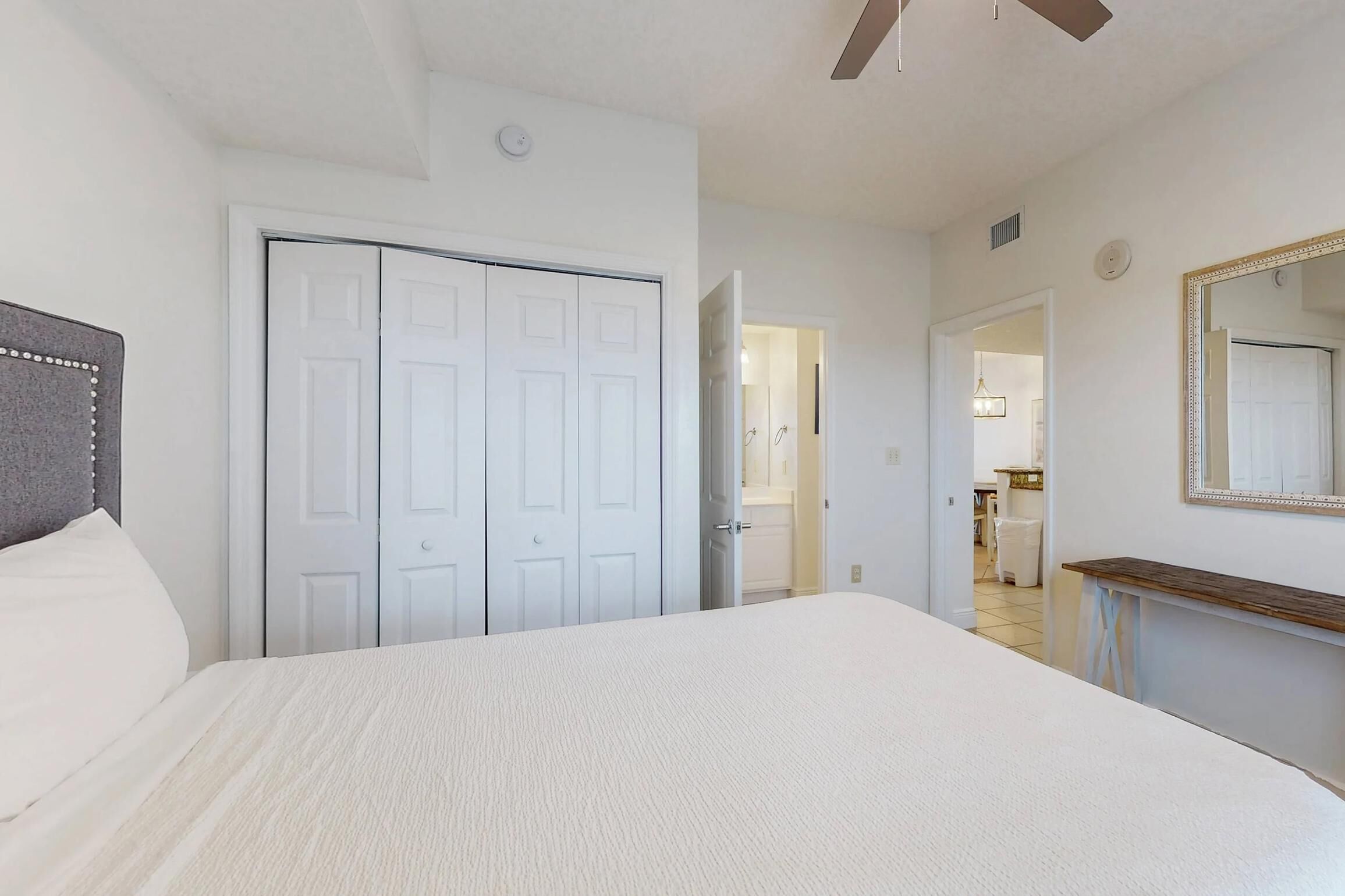 A bedroom with a bed, a wardrobe, a mirror, and a hallway leading to a bathroom.