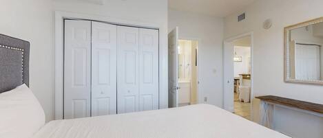 A bedroom with a bed, a wardrobe, a mirror, and a hallway leading to a bathroom.