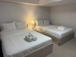Ein Hotelzimmer mit zwei Betten, jeweils mit weißer Bettwäsche und Kissen, einem Nachttisch mit Lampe und einem aufgerollten Handtuch auf dem Bett.