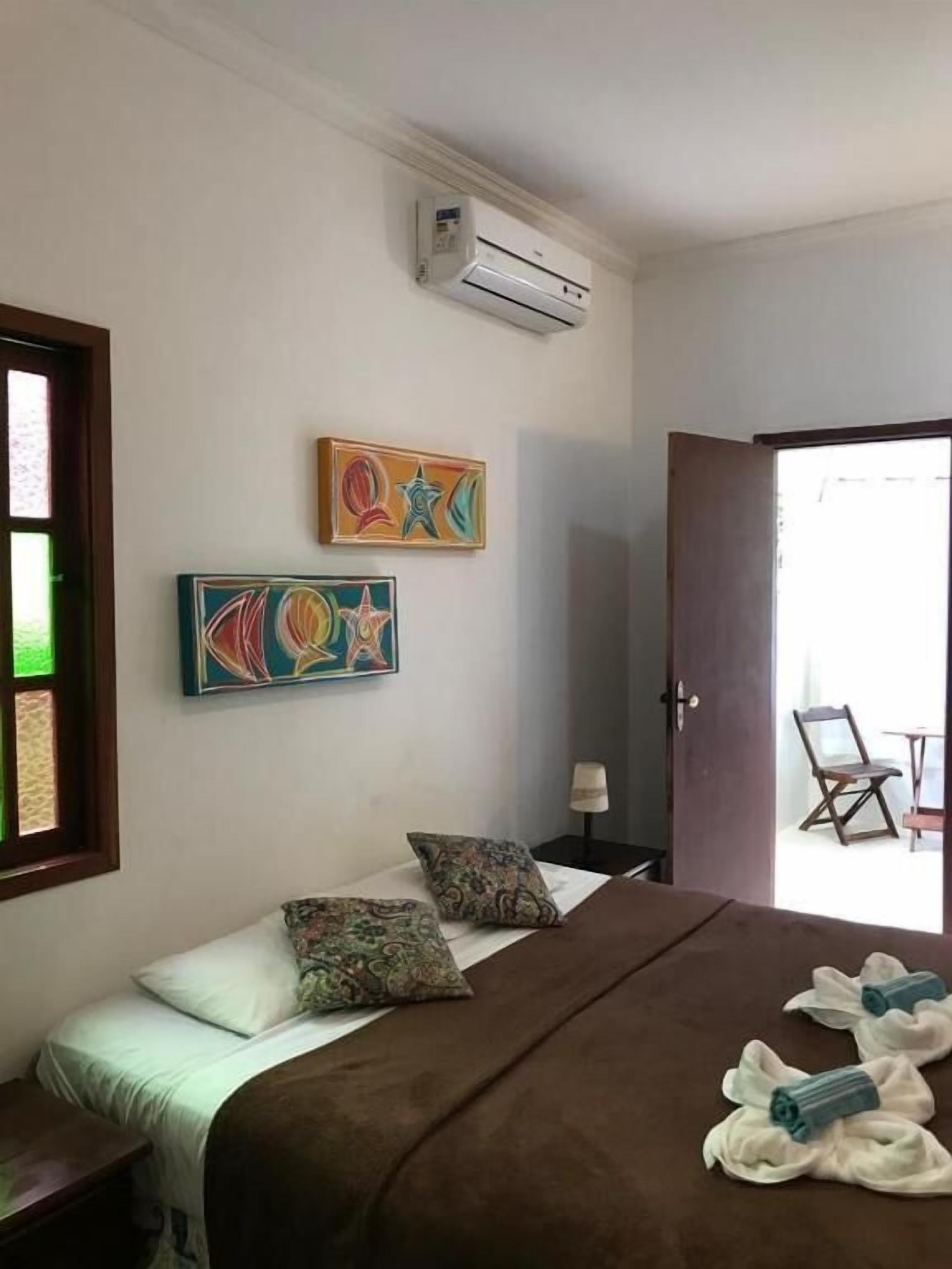 A bedroom with a bed, pillows, an air conditioner, and artwork on the wall.