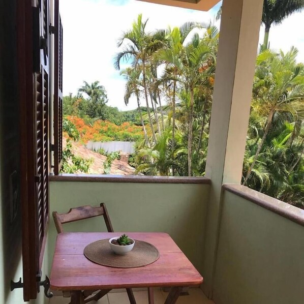 Un balcón con una mesa y una silla, un frutero con fruta y vistas a palmeras y follaje.