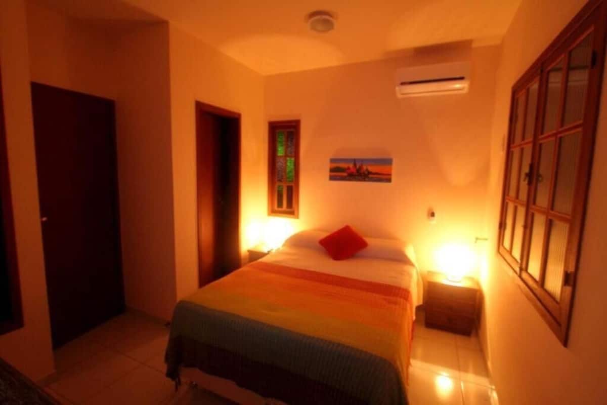 Ein Hotelzimmer mit Bett, Nachttischen, Klimaanlage, einer Tür und einem Fenster mit Aussicht.