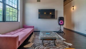 A modern room with a pink sofa, a zebra-patterned rug, a mounted TV, and a speaker on a tripod. - Holiday Lofts NYC (Newark)