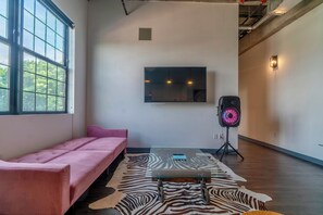 A modern room with a pink sofa, a zebra-patterned rug, a mounted TV, and a speaker on a tripod. - Holiday Lofts NYC (Newark)