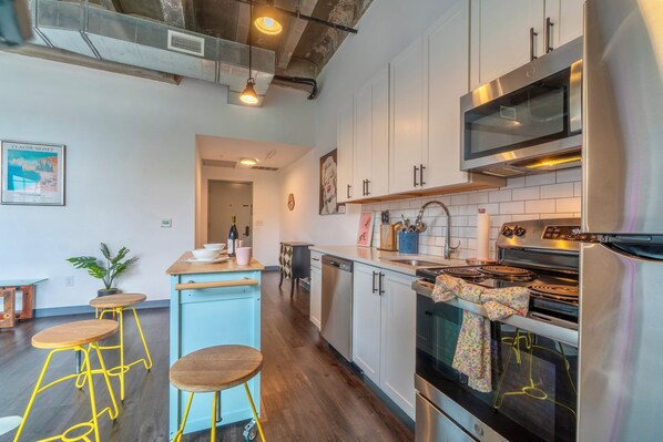 A modern kitchen with stainless steel appliances, a wooden dining area, and a bar stool. - Holiday Lofts NYC (Newark)