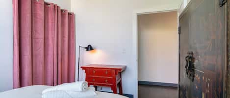 A hotel room with a bed, a red dresser, a lamp, and a wardrobe.