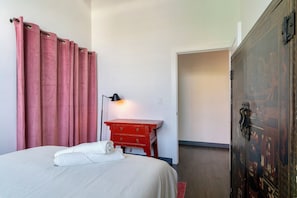 A hotel room with a bed, a red dresser, a lamp, and a wardrobe. - Holiday Lofts NYC (Newark)