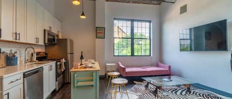 A compact kitchen with modern appliances, a dining area with a zebra-patterned rug, and a cozy seating area with a pink sofa.