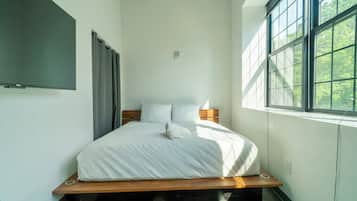 A modern bedroom with a wooden platform bed, white bedding, and a large window with a view of trees.