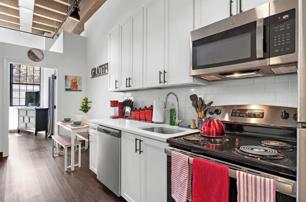 A modern kitchen with white cabinets, stainless steel appliances, and a red kettle on the stove.