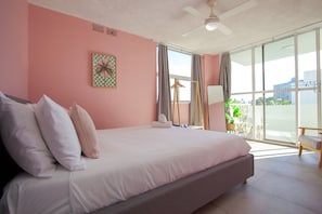 Une chambre avec un grand lit, un ventilateur de plafond, une fenêtre avec des rideaux et une vue sur l’extérieur.