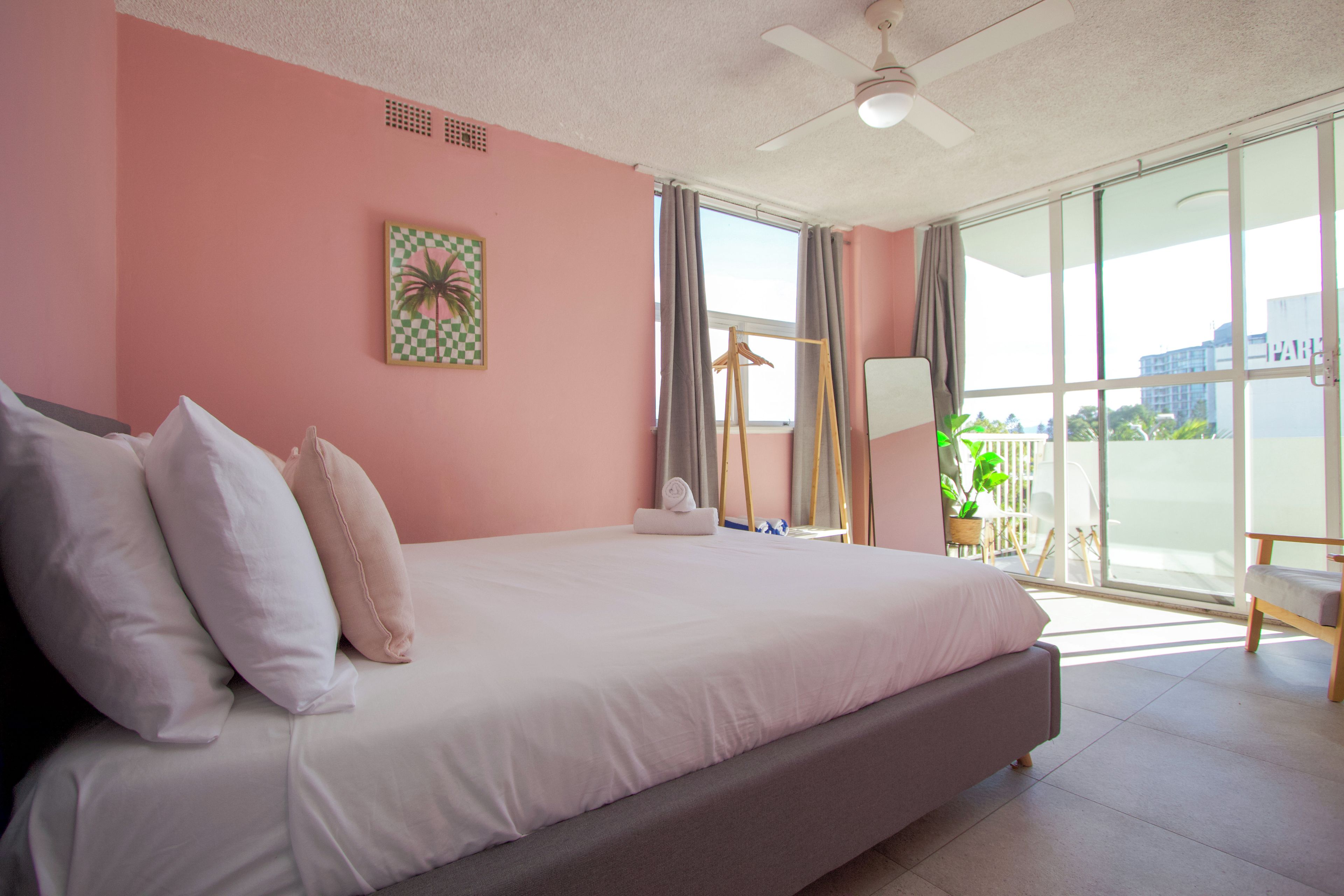 A bedroom with a large bed, a ceiling fan, a window with curtains, and a view of the outside.