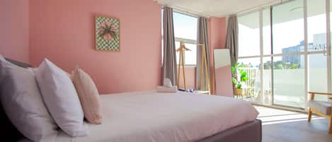 A bedroom with a large bed, a ceiling fan, a window with curtains, and a view of the outside.