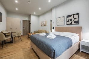 A hotel room with a bed, a desk, a chair, a wardrobe, and artwork on the walls. - Raise Heraklion 4 Moments (Heraklion)
