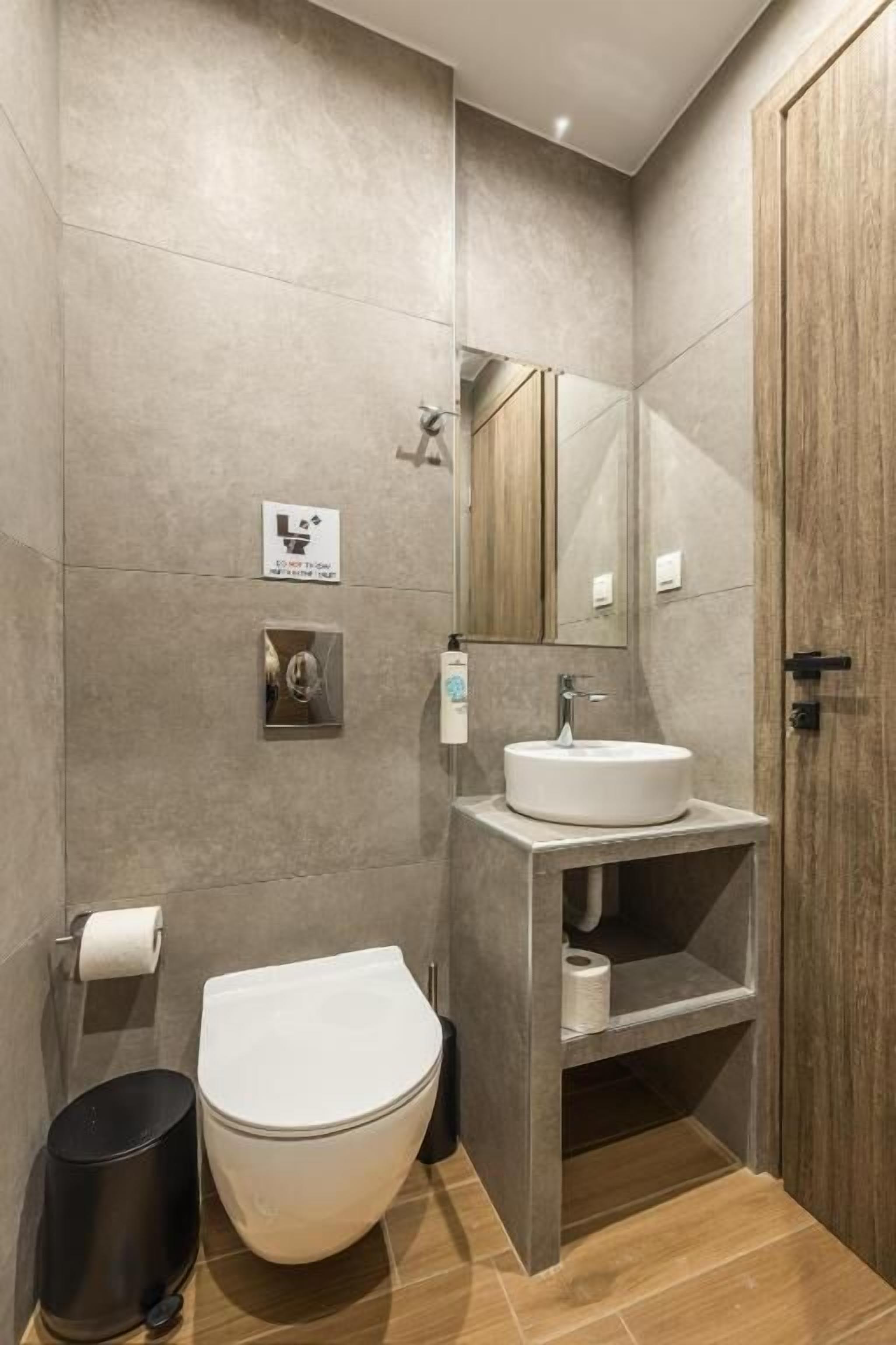 Ein modernes Badezimmer mit Toilette, Waschbecken, Spiegel und Holztür.
