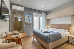 A modern hotel room with a bed, bedside table, and a dining area with a table and chairs. - Raise Heraklion 4 Moments (Heraklion)