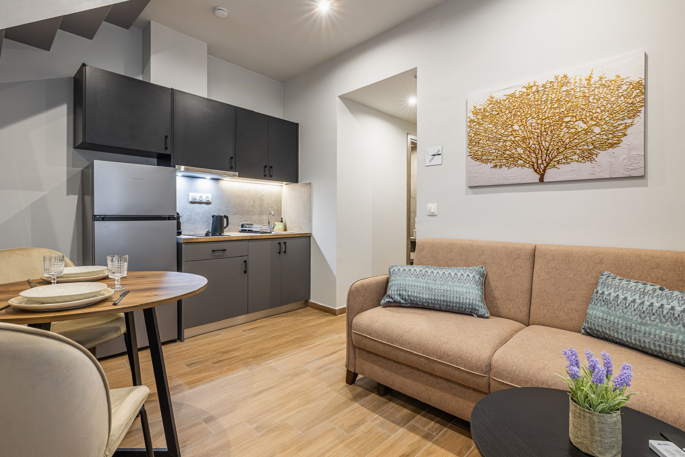 Et moderne køkken med mørke skabe, et spisebord med stole, og en opholdsstue med sofa og sofabord.