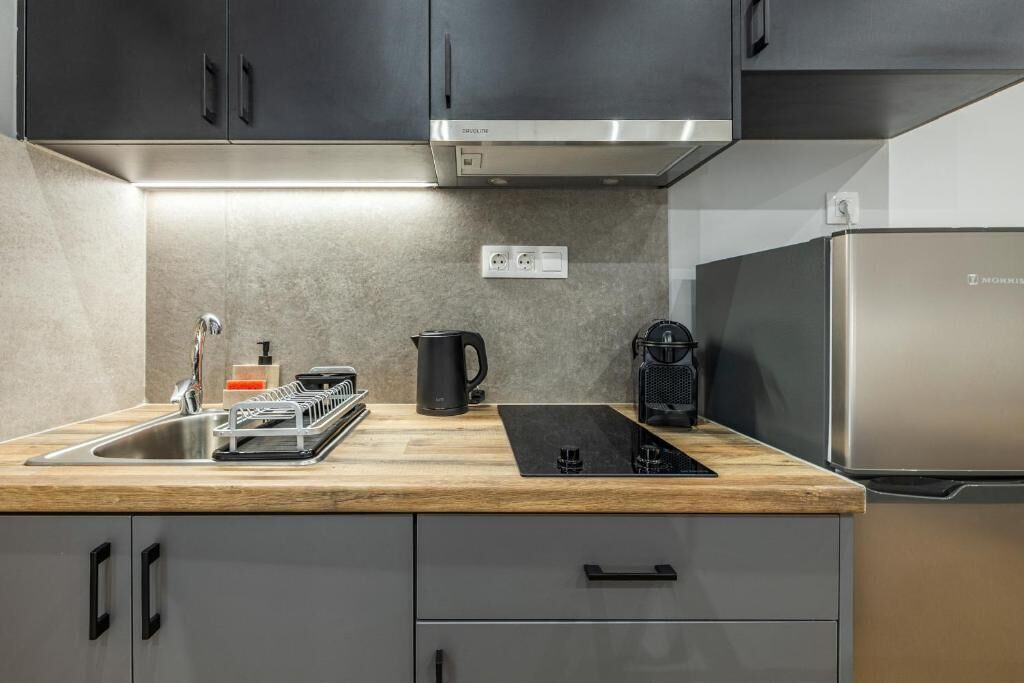 A modern kitchen with stainless steel appliances, a wooden countertop, and grey cabinetry.