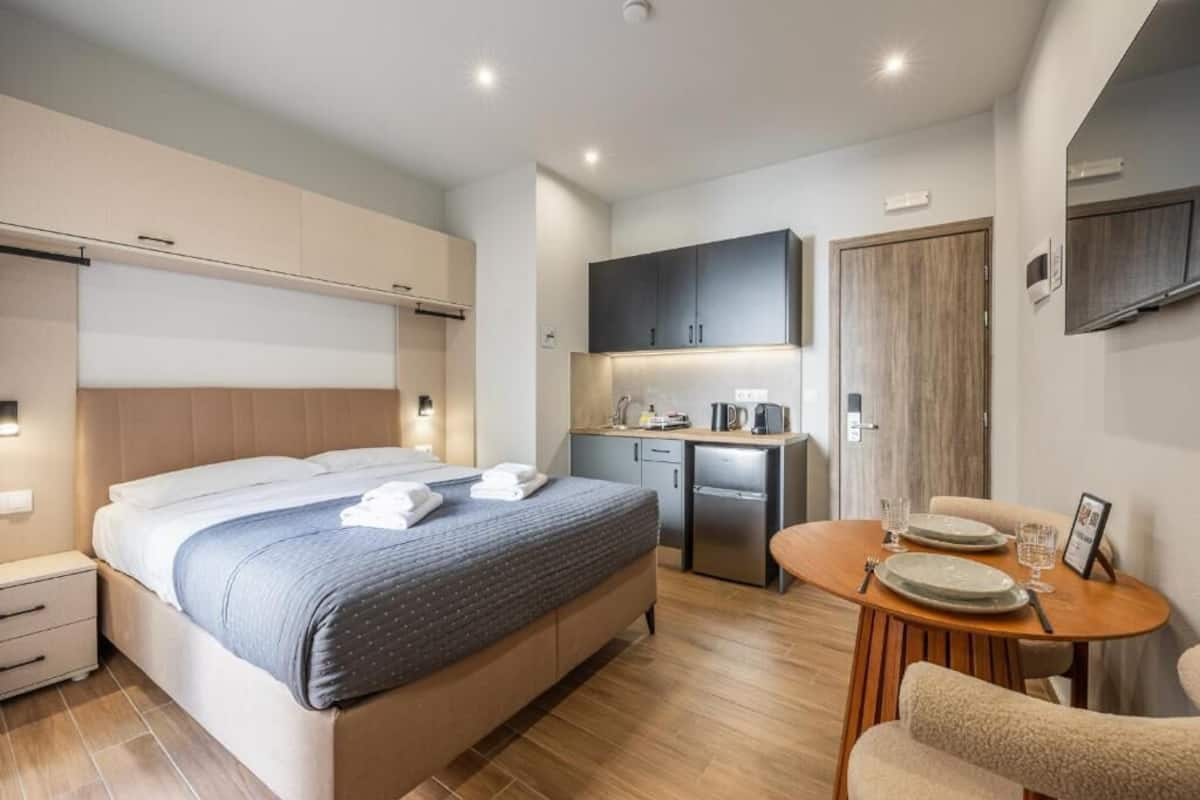 Una habitación de hotel moderna con cama, una kitchenette pequeña, una mesa de comedor con sillas y un baño independiente.