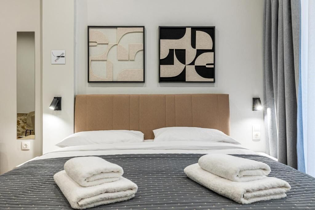 A hotel room with a bed, two wall-mounted abstract art pieces, a headboard, and a window with curtains.