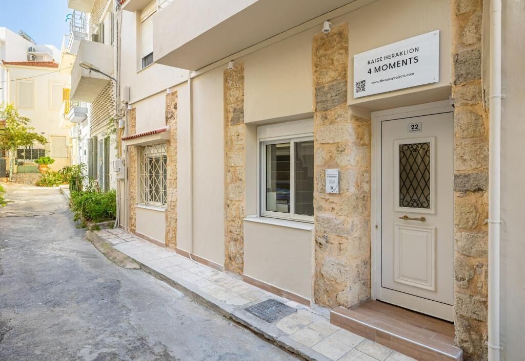Een woongebouw met een stenen gevel, een deur met het nummer '22' en een bordje met de tekst 'RAISE HERAKLION 4 MOMENTS'.