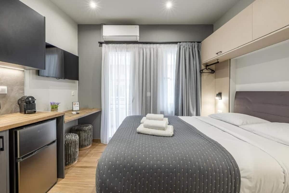 Habitación de hotel moderna con cama, kitchenette pequeña, televisión de pantalla plana y ventana con cortinas.