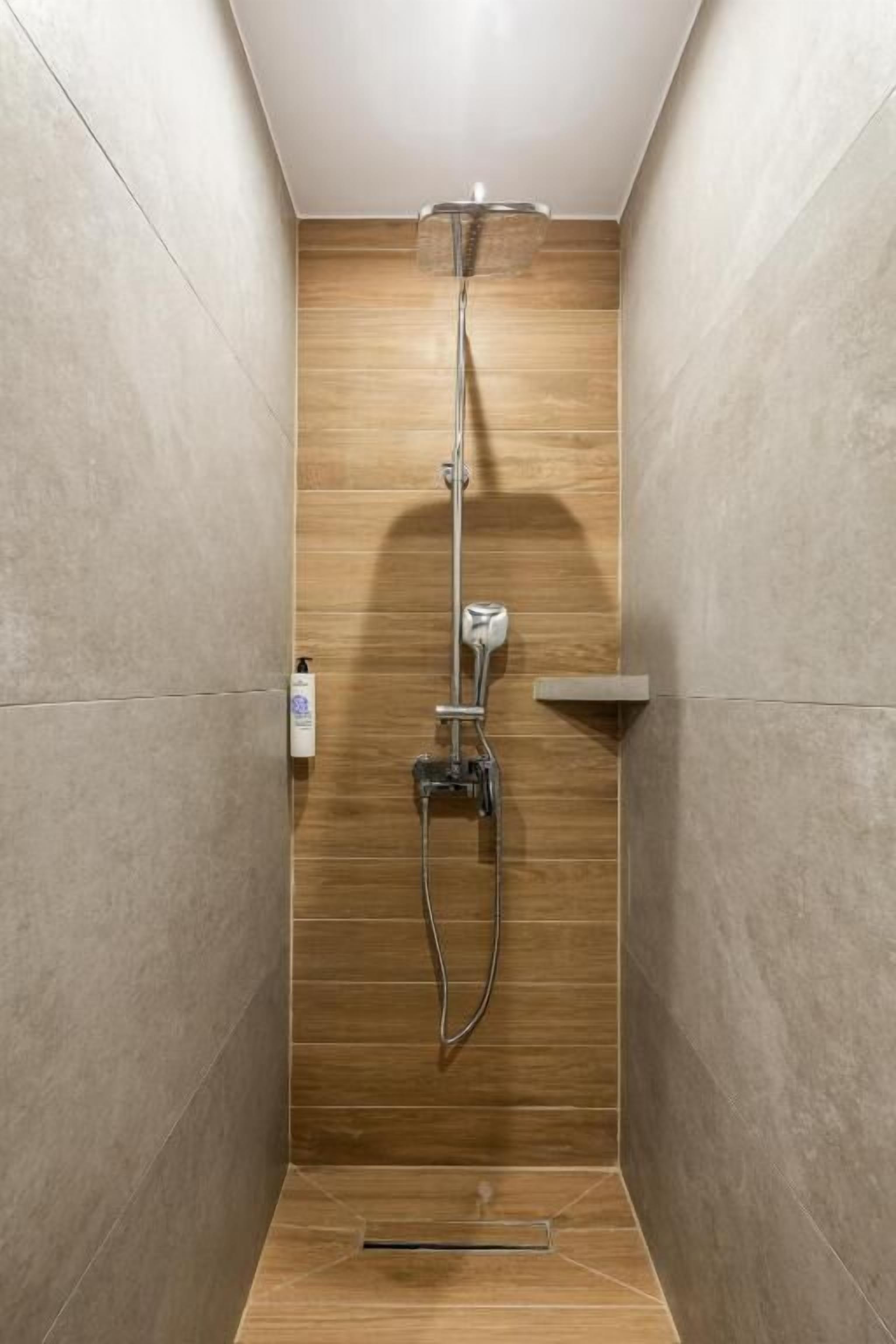 A shower with a handheld showerhead, a wall-mounted faucet, and a handheld showerhead.