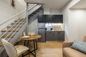 Et kompakt køkken med moderne hårde hvidevarer, et spiseområde med et bord og stole, og en trappe til et andet niveau.