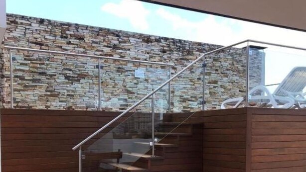 Een moderne trap met een stenen muur, houten lambrisering en een glazen balustrade.