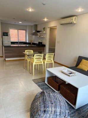 A modern living room with a dining area, a kitchen in the background, and a large window. - Shopping del Sol Zone (Asunción)