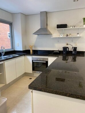A modern kitchen with a large island, built-in oven, and stainless steel range hood. - Shopping del Sol Zone (Asunción)