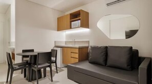 Quarto moderno com mesa de jantar, cadeiras, sofá, cozinha planejada com micro-ondas e um espelho grande.