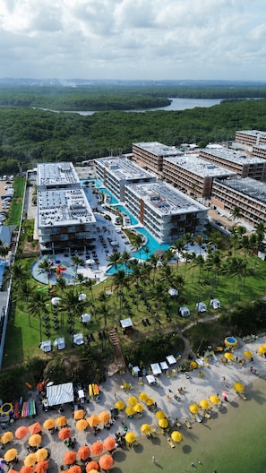 Un complexe hÎtelier comprenant plusieurs bùtiments, une piscine centrale et une plage aménagée avec des parasols.