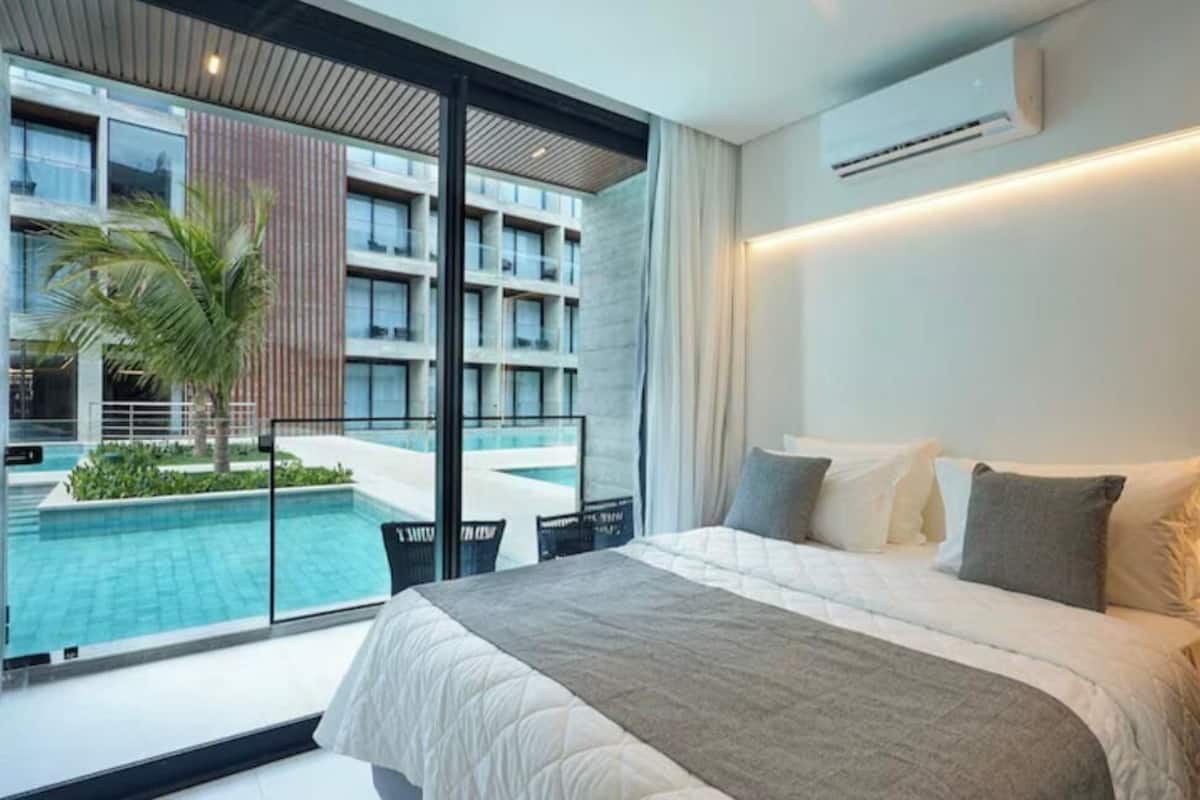 A modern hotel room with a large bed, a view of a swimming pool, and a balcony.