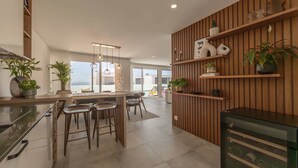 Een moderne keuken met een centraal eiland, een paar barkrukken, houten planken met planten en een wijnkoeler.