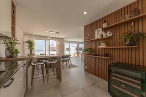 Eine moderne Küche mit einer zentralen Kochinsel, Barhocker, Holzregalen mit Pflanzen und einem Weinkühlschrank.