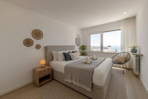 Ein modernes Schlafzimmer mit einem großen Bett, Nachttischen, einem Sessel und Meerblick.