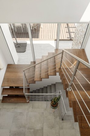 Eine moderne Treppe mit Holzhäuschen und Metallgeländern, die zu einem Außenbereich mit einer Holzdielenfläche und einem Blumentopf führt.