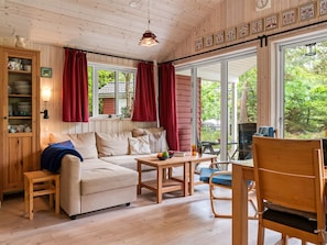 Ein gemütliches Zimmer mit einer Couch, einem Tisch, einem Stuhl, einem Schrank mit Geschirr und einem Fenster mit Vorhängen.