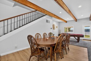 Ein Essbereich mit Holztisch und -stühlen, einem Billardtisch und einer Treppe mit Holzbalken.