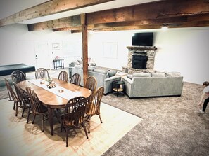 A dining area with a wooden table and chairs, a gray sofa, and a stone fireplace.