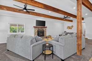 Ein Wohnzimmer mit Kamin aus Stein, zwei grauen Sofas, einem kleinen runden Tisch und einem Deckenventilator.