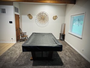 A room with a massage table, a chair, decorative wall art, a window with blinds, and a door.
