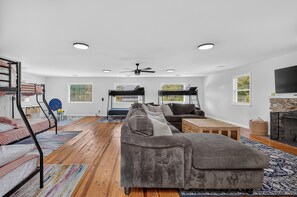 Ein modernes Wohnzimmer mit einer Couch, einem Couchtisch und einem Kamin. Links befinden sich Etagenbetten und rechts ein Fernseher.