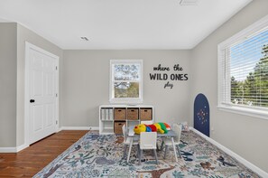 Ein Kinderzimmer mit Teppich, einem weißen Schreibtisch, einem Stuhl, einem Bücherregal und einer Wand mit einem Poster zum Thema Tierwelt.