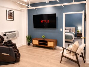 Ett modernt vardagsrum med en platt-TV på väggen som visar logotypen för ”NETFLIX”, en soffa, ett soffbord och en massagefåtölj.
