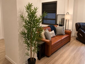 Ein Wohnzimmer mit braunem Ledersofa, einer großen Kübelpflanze mit Bambus, einem Massagesessel und einem an der Wand befestigten Fernseher.