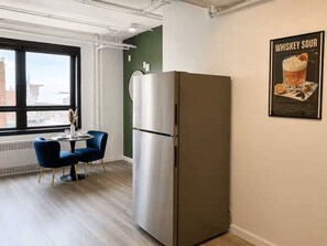 Eine moderne Küche mit einem Edelstahl-Kühlschrank, einem Essbereich mit blauem Stuhl und Tisch sowie einem großen Fenster mit Blick auf die Stadt.