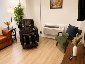 Ein Massagesessel, ein Sofa, ein grüner Sessel, eine Fernbedienung und eine Wand-Klimaanlage.